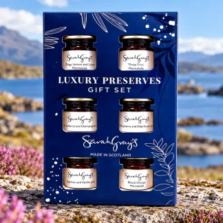 Sarah Gray’s Luxury Scottish Preserves Gift Set with six mini jars of jams and marmalades in a navy gift box, photographed against a Scottish coastal landscape.