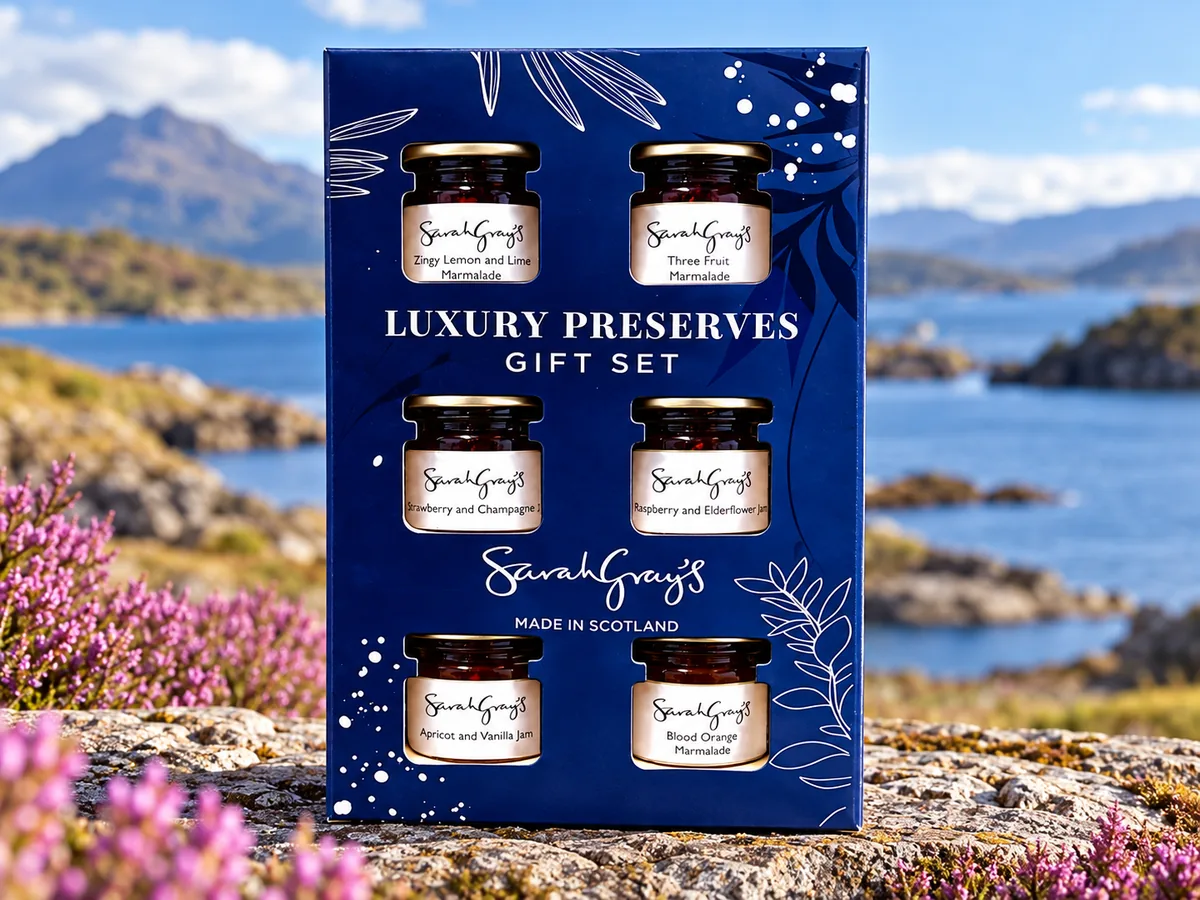 Sarah Gray’s Luxury Scottish Preserves Gift Set with six mini jars of jams and marmalades in a navy gift box, photographed against a Scottish coastal landscape.